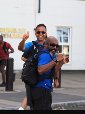 two men wearing matching blue shirts and black shorts both with thumbs up happy expressions running