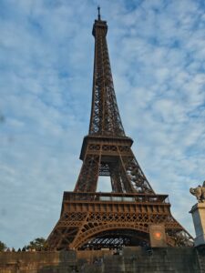 A dramatic upward view of the Eiffel Tower in Paris against a blue sky with scattered clouds.